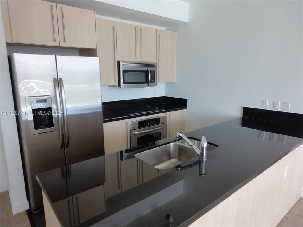 A kitchen features light wood cabinets, stainless steel appliances, and a black countertop island — 79 SW 12th St # 1203S, Miami FL 33130, MIAMI, FL