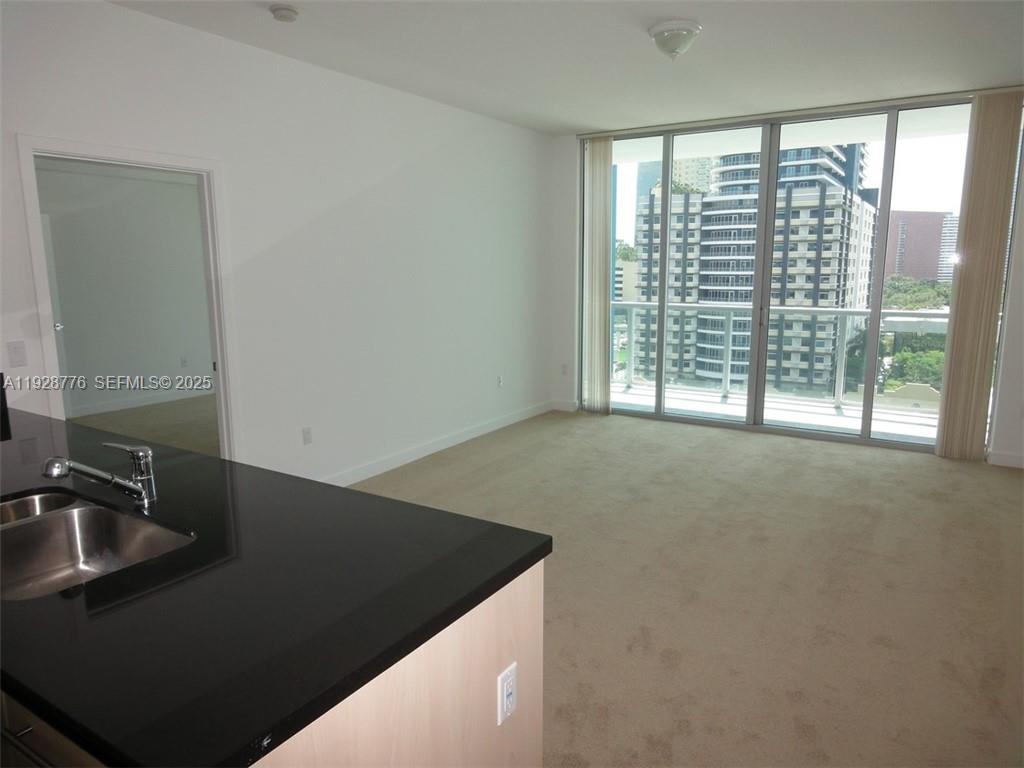 An interior view shows a carpeted living area with floor-to-ceiling windows and a kitchen counter — 79 SW 12th St # 1203S, Miami FL 33130, MIAMI, FL