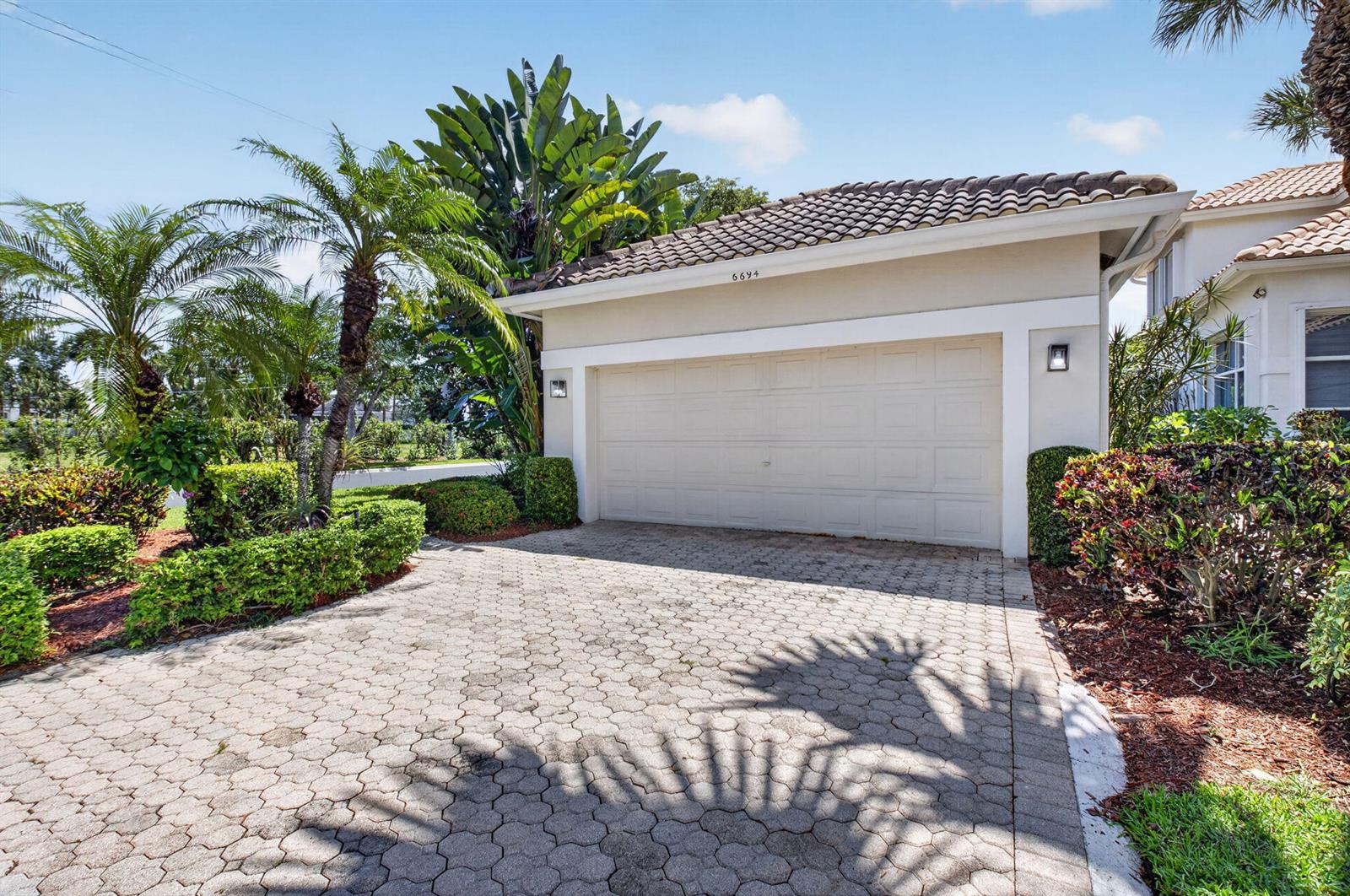 A paved driveway leads to a single-story garage with a tiled roof and palm trees — 6694 NW 26th Way, Boca Raton FL 33496, BOCA RATON, FL