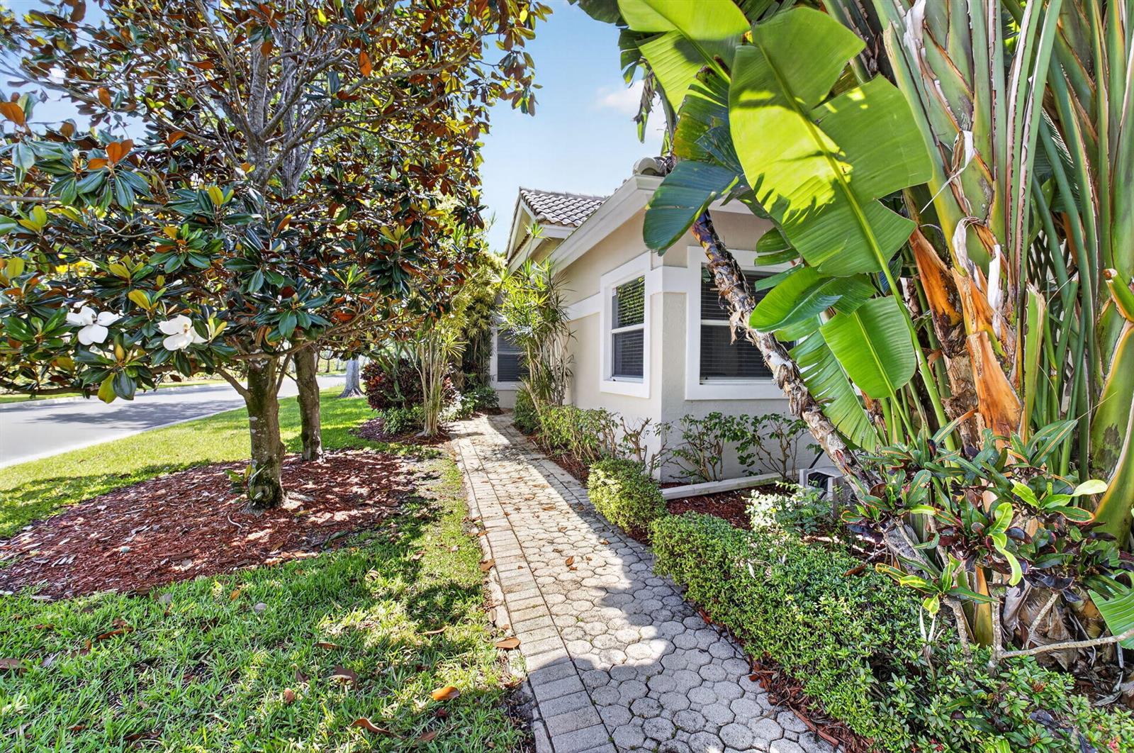 A paved walkway leads past a house exterior with lush landscaping and a large tree — 6694 NW 26th Way, Boca Raton FL 33496, BOCA RATON, FL