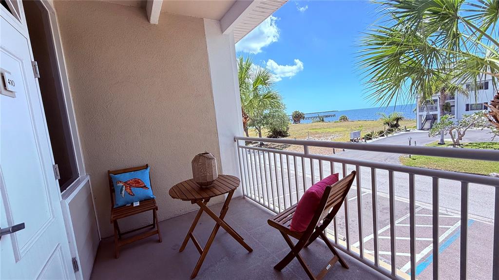 A balcony with a small wooden table and two chairs overlooks a parking lot and ocean — 611 DESTINY DRIVE UNIT 410, RUSKIN, FL