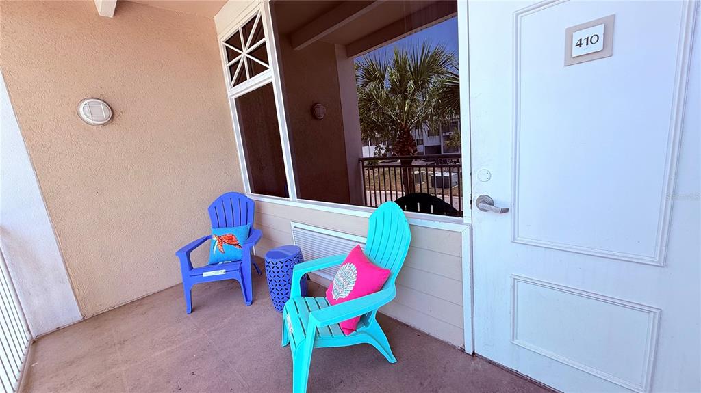 A balcony features two blue Adirondack chairs with colorful pillows and a small side table — 611 DESTINY DRIVE UNIT 410, RUSKIN, FL