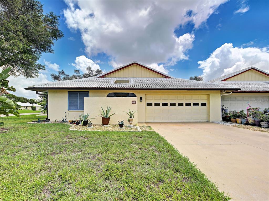 A single-story house with a light-colored exterior, a two-car garage, and a landscaped front yard — 20 IDLE SANDS DRIVE, VENICE, FL