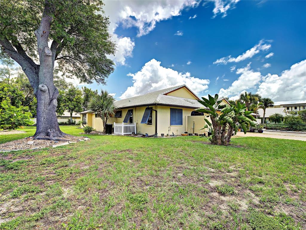 A yellow house with a tile roof sits on a grassy lot with large trees — 20 IDLE SANDS DRIVE, VENICE, FL