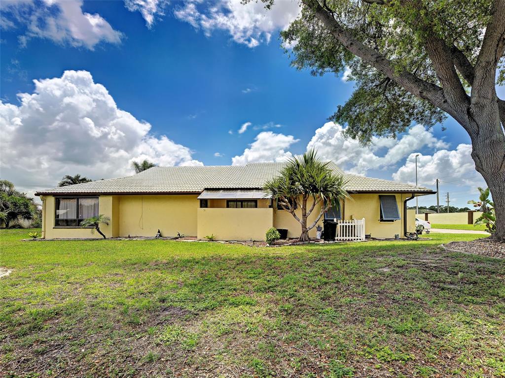 A yellow single-story house with a tiled roof sits on a grassy lawn — 20 IDLE SANDS DRIVE, VENICE, FL