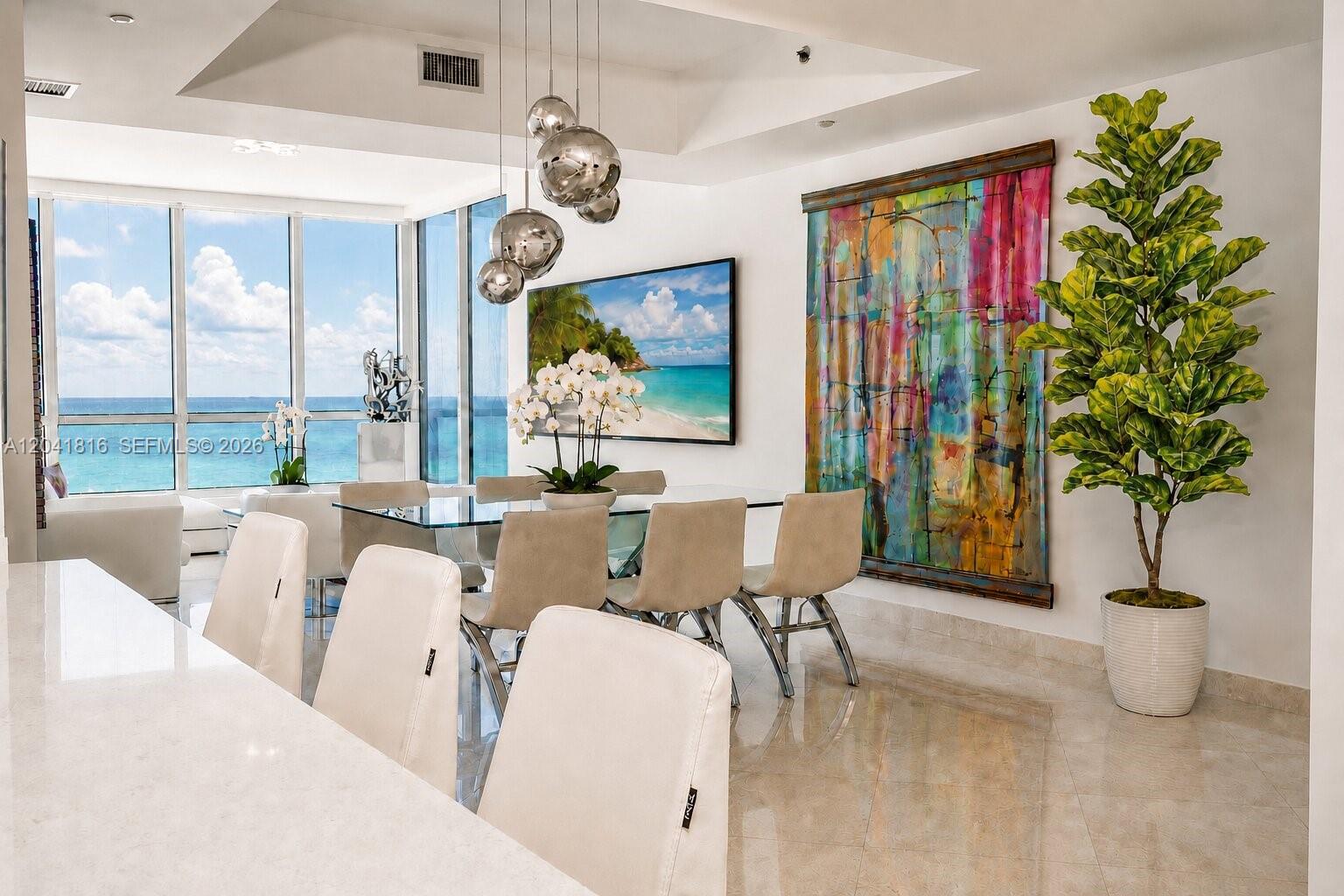 A dining room features a glass table, modern chairs, pendant lights, and ocean views — 100 S Pointe Dr # 1507, Miami Beach FL 33139, MIAMI BEACH, FL