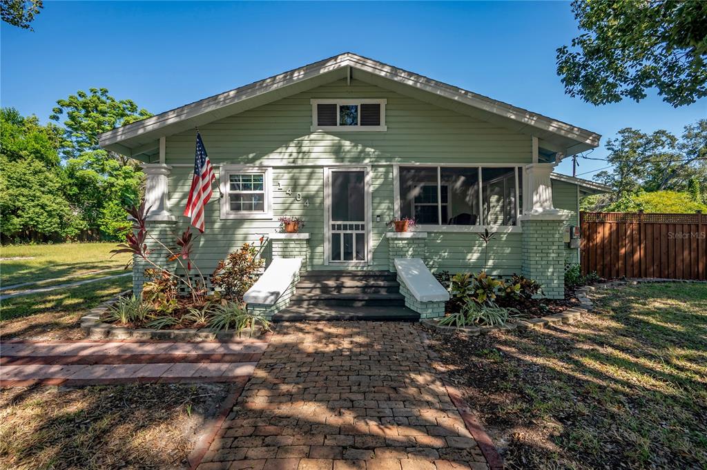 A light green bungalow with a brick walkway, front porch, and an American flag — 1404 E CAYUGA STREET, TAMPA, FL