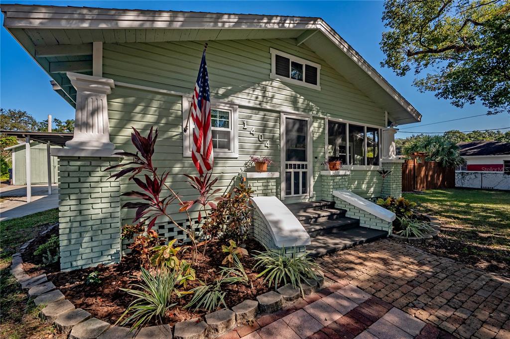 A light green bungalow with a brick foundation, front porch, and an American flag — 1404 E CAYUGA STREET, TAMPA, FL