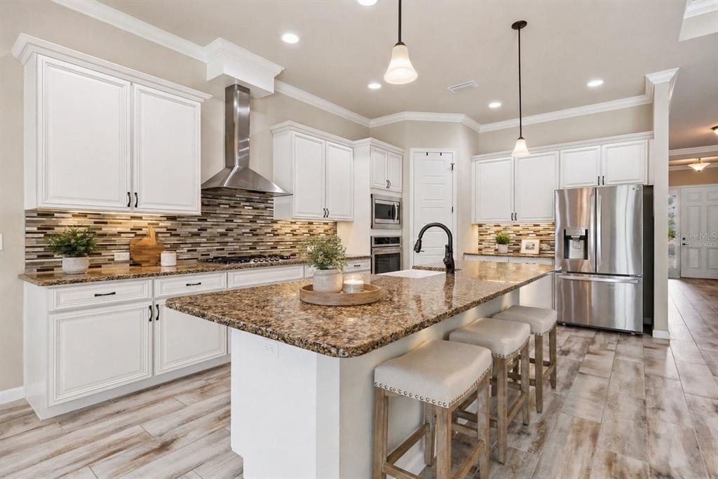 A kitchen features white cabinetry, granite countertops, a stainless steel range hood, and a center island — 1061 NW 134TH DRIVE, NEWBERRY, FL