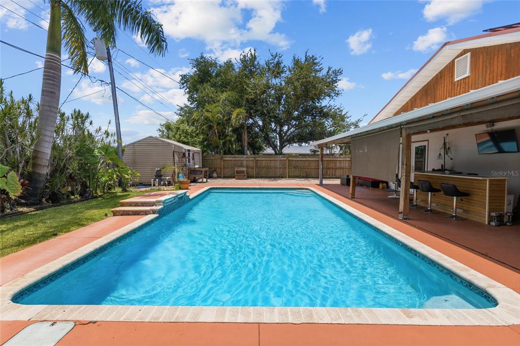 A rectangular swimming pool sits in a backyard with a covered patio and bar area — 311 62ND STREET W, BRADENTON, FL