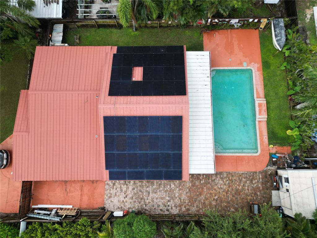 An aerial view shows a house with a metal roof, solar panels, and a swimming pool — 311 62ND STREET W, BRADENTON, FL