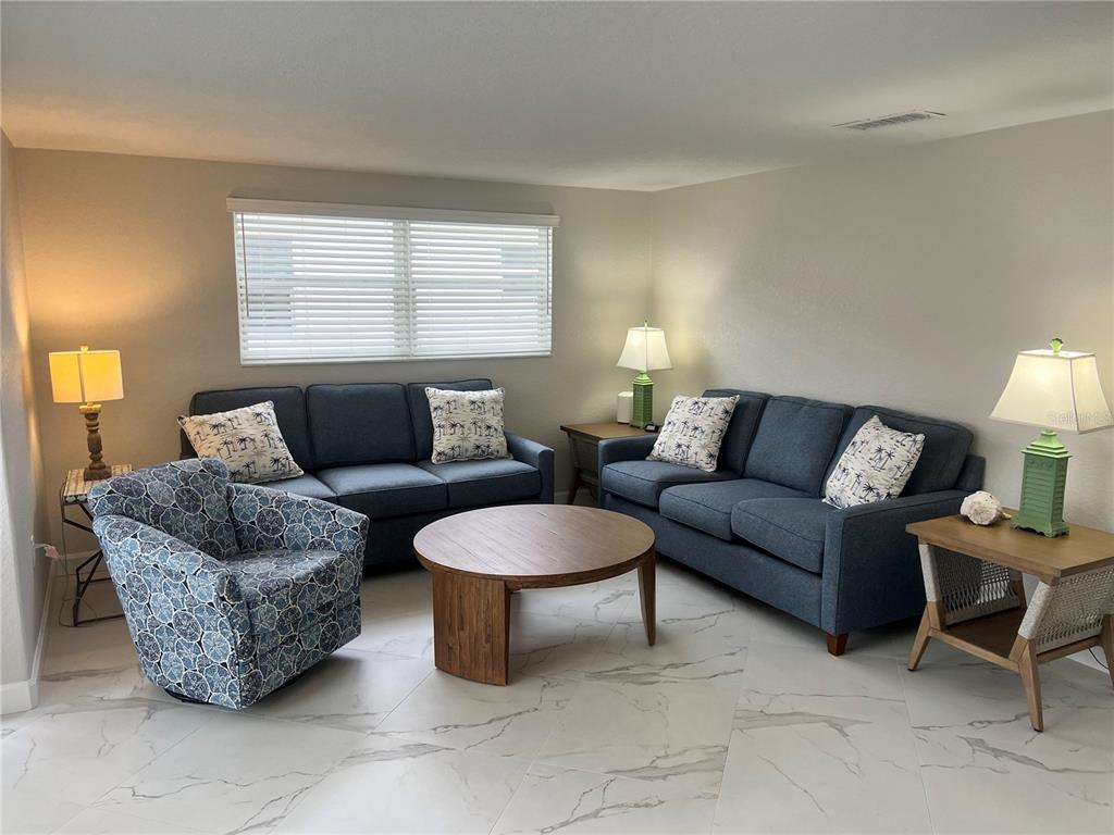 A living room features two blue sofas, a patterned armchair, and a round wooden table — 6154 MIDNIGHT PASS ROAD UNIT B14, SARASOTA, FL