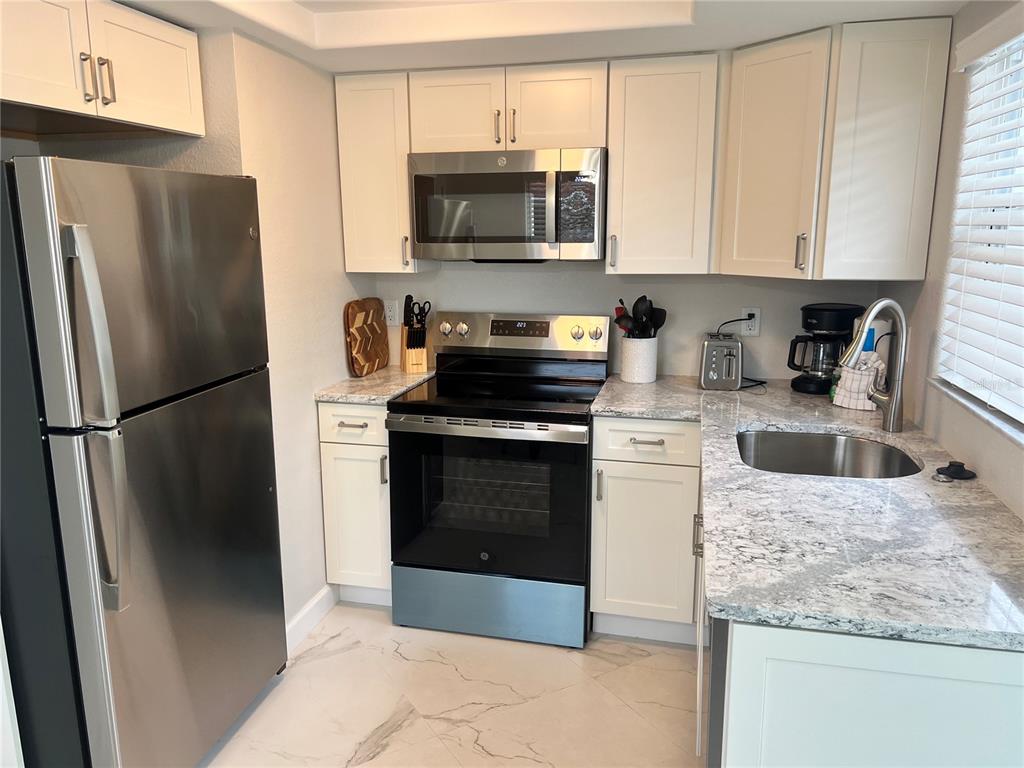 A kitchen features white cabinets, stainless steel appliances, and granite countertops with a tile floor — 6154 MIDNIGHT PASS ROAD UNIT B14, SARASOTA, FL