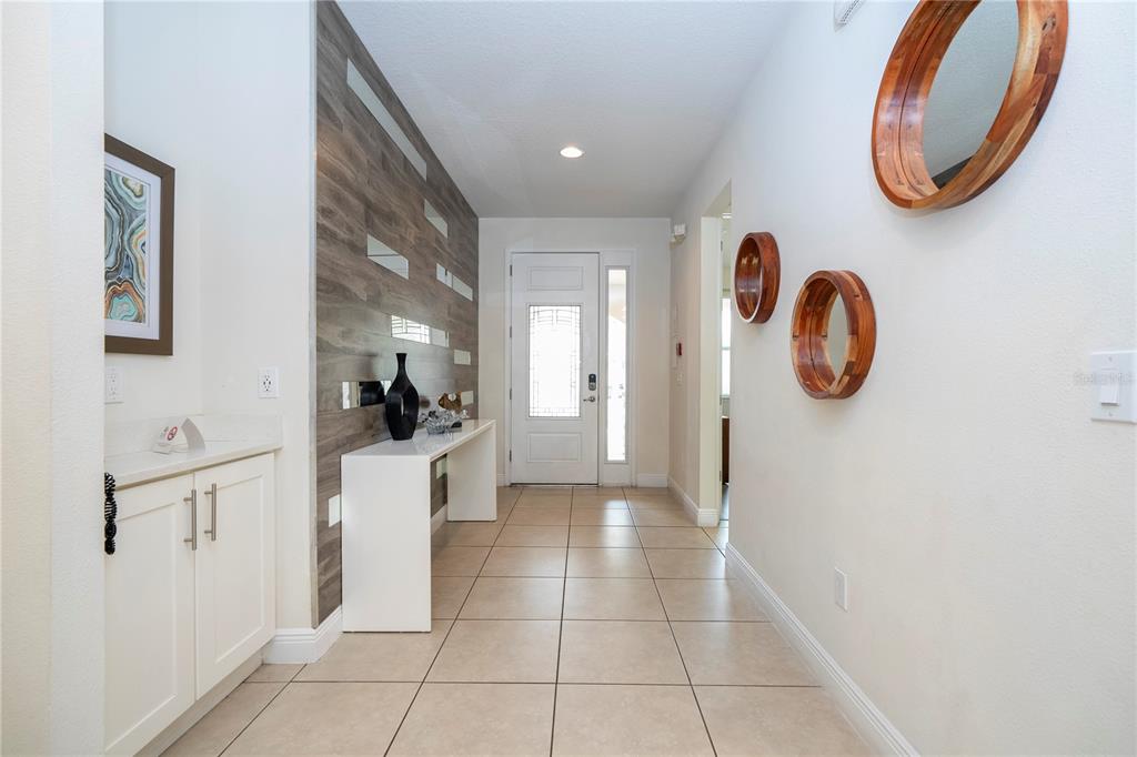 An entryway features tile flooring, a wood-paneled accent wall, a white console table, and mirrors — 7600 MACKINAW LANE, KISSIMMEE, FL