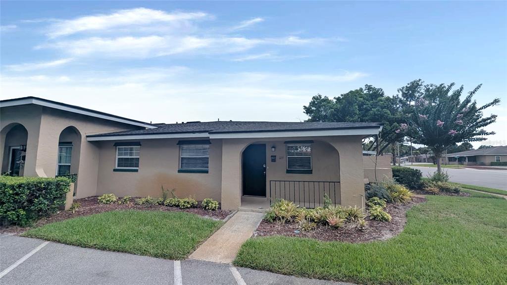 A tan single-story building features a covered entryway, dark trim, and a small landscaped yard — 519 POLARIS LOOP UNIT 109, CASSELBERRY, FL