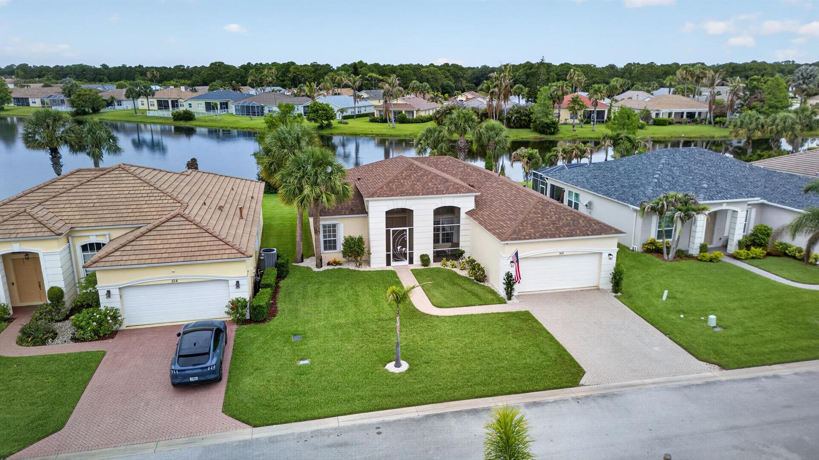 An aerial view shows two suburban houses with tile roofs, green lawns, and a lake — 512 SW Lake Manatee Way, FL 34986, FL