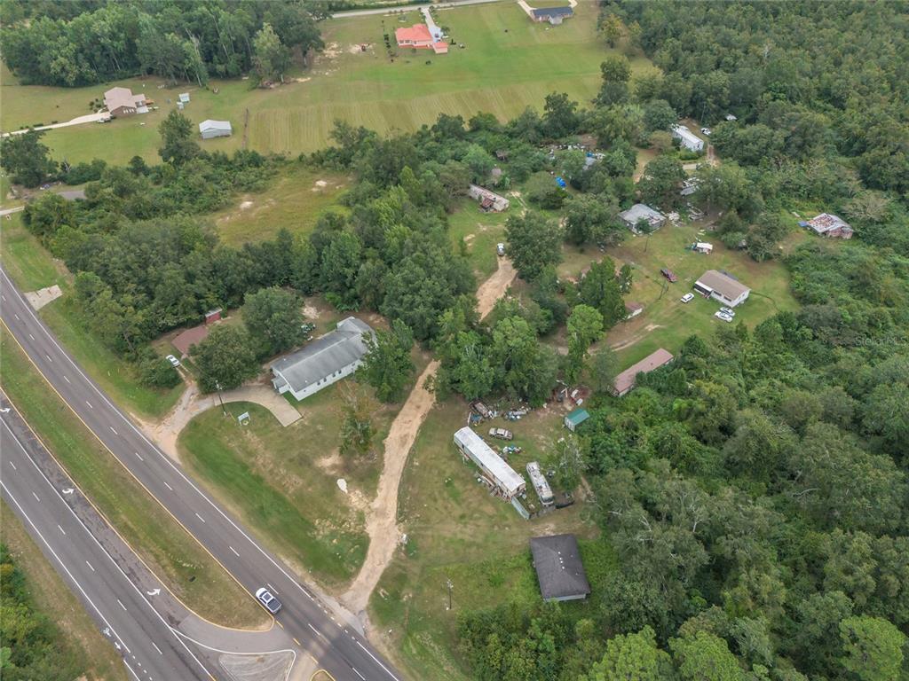 An aerial view shows a rural property with multiple buildings, a dirt driveway, and surrounding woods — 465 HAZZARD LANE, CANTONMENT, FL