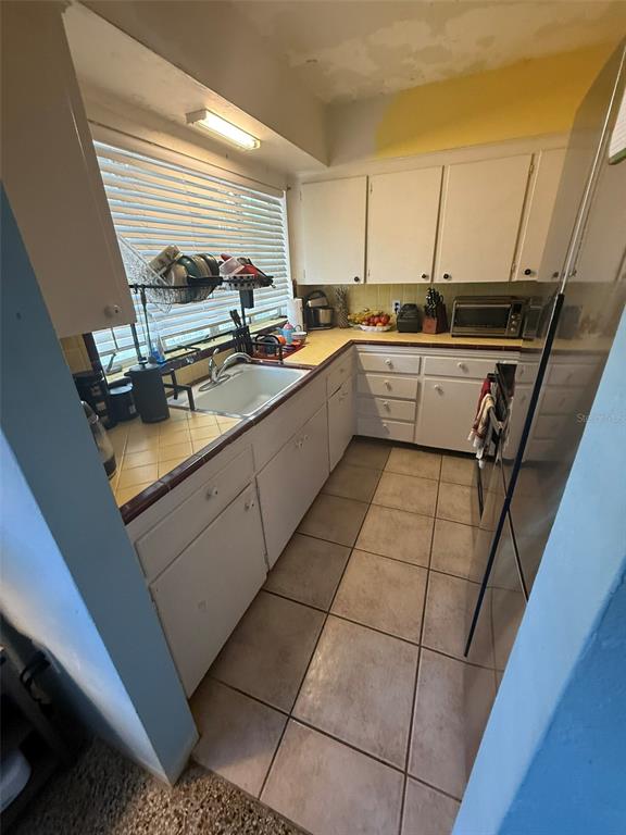 A galley kitchen features white cabinets, tiled countertops, a stainless steel sink, and tile flooring — 316 76TH AVENUE, ST PETE BEACH, FL