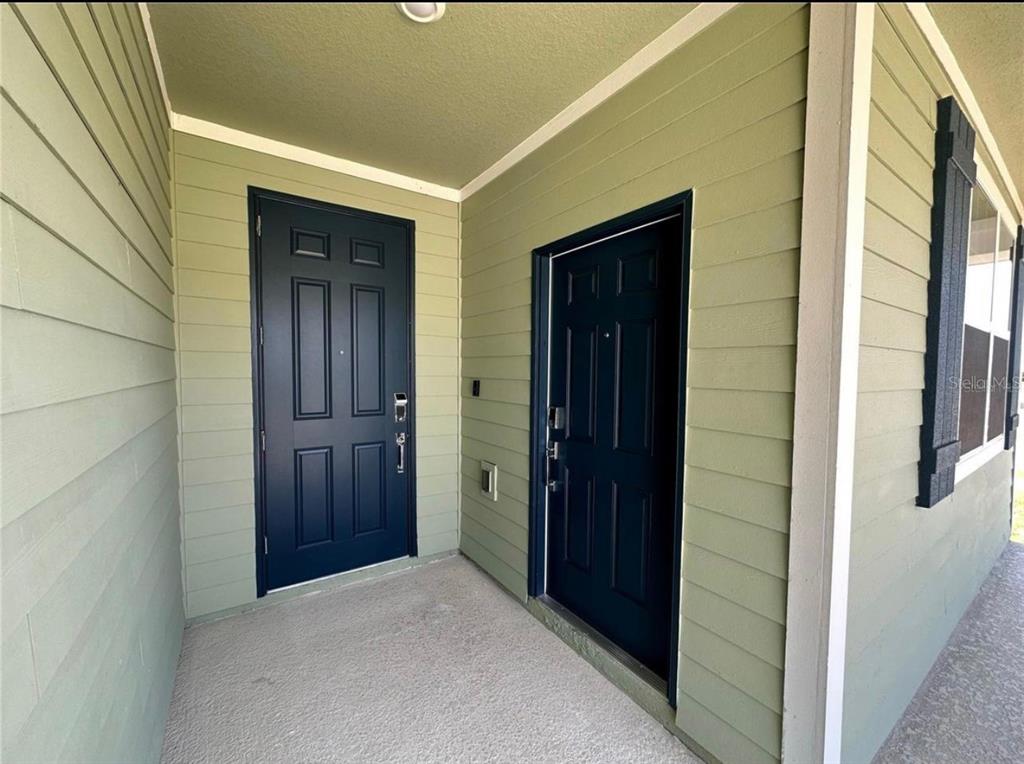 A covered entryway features two dark blue doors set against light green horizontal siding — 4500 BLUFF OAK LOOP UNIT 1, KISSIMMEE, FL