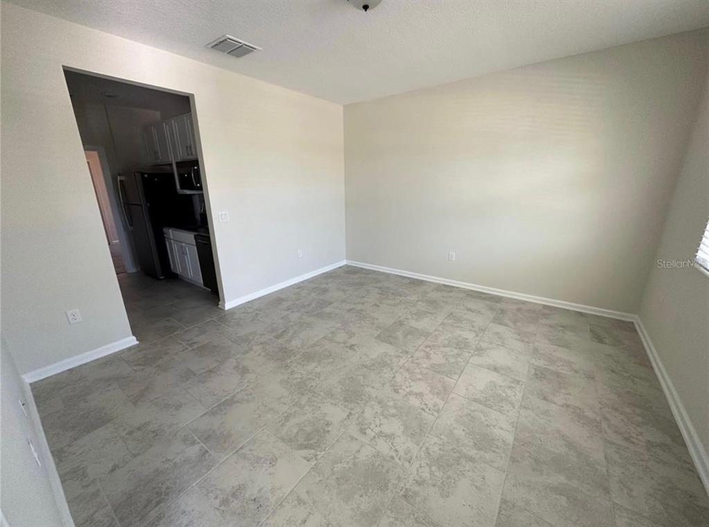 A room with light-colored walls and grey tile flooring leads into a kitchen — 4500 BLUFF OAK LOOP UNIT 1, KISSIMMEE, FL