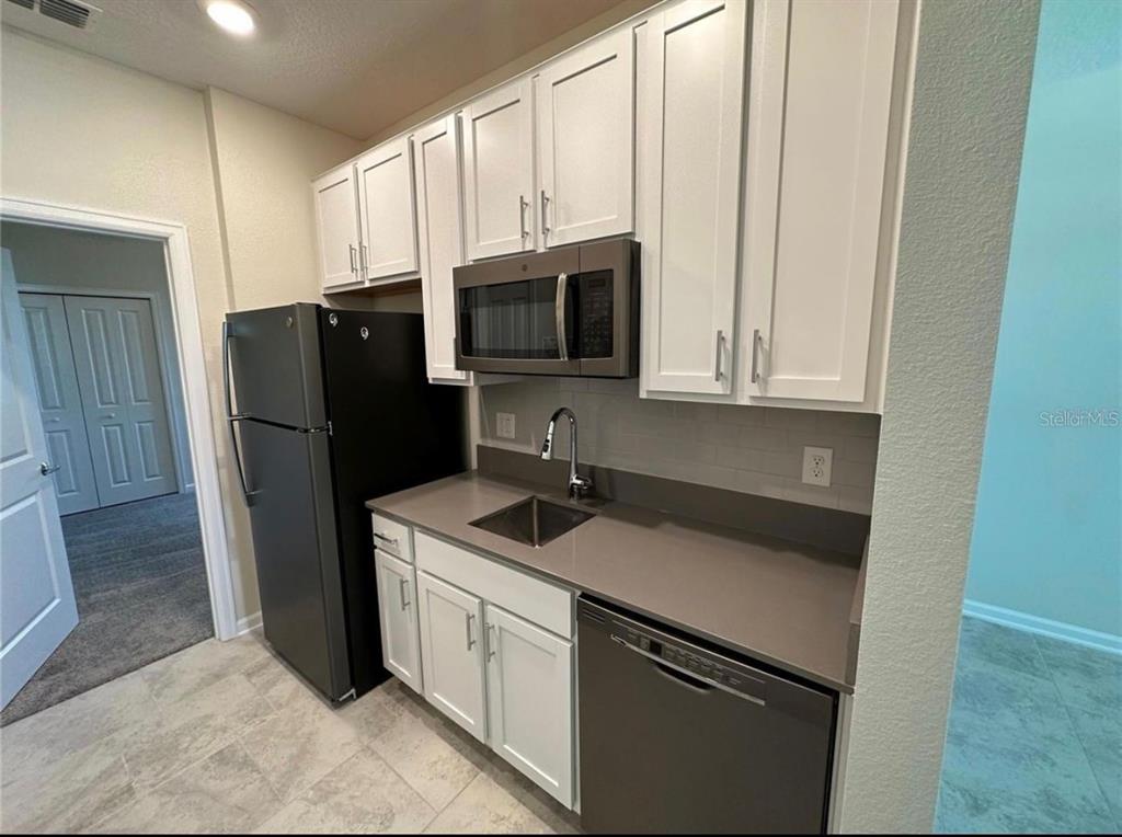 A kitchen features white cabinets, dark countertops, a black refrigerator, and a stainless steel dishwasher — 4500 BLUFF OAK LOOP UNIT 1, KISSIMMEE, FL
