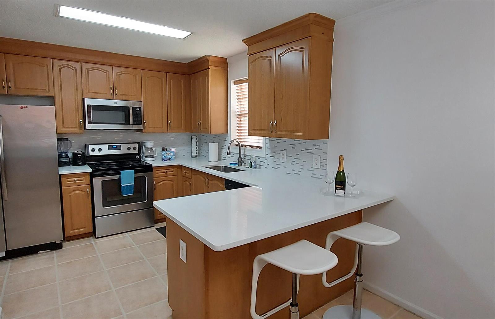 A kitchen features wood cabinets, stainless steel appliances, white countertops, and a breakfast bar — 1401 W 9th Street, Riviera Beach FL 33404, RIVIERA BEACH, FL