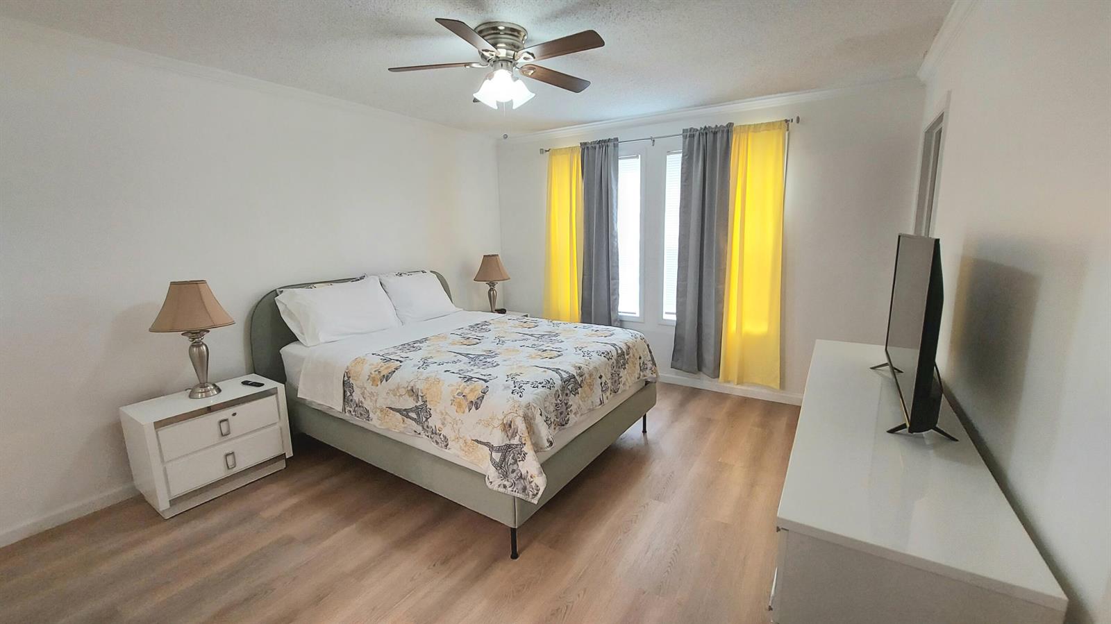 A bedroom features a bed with a patterned comforter, white nightstands, and yellow-gray curtains — 1401 W 9th Street, Riviera Beach FL 33404, RIVIERA BEACH, FL