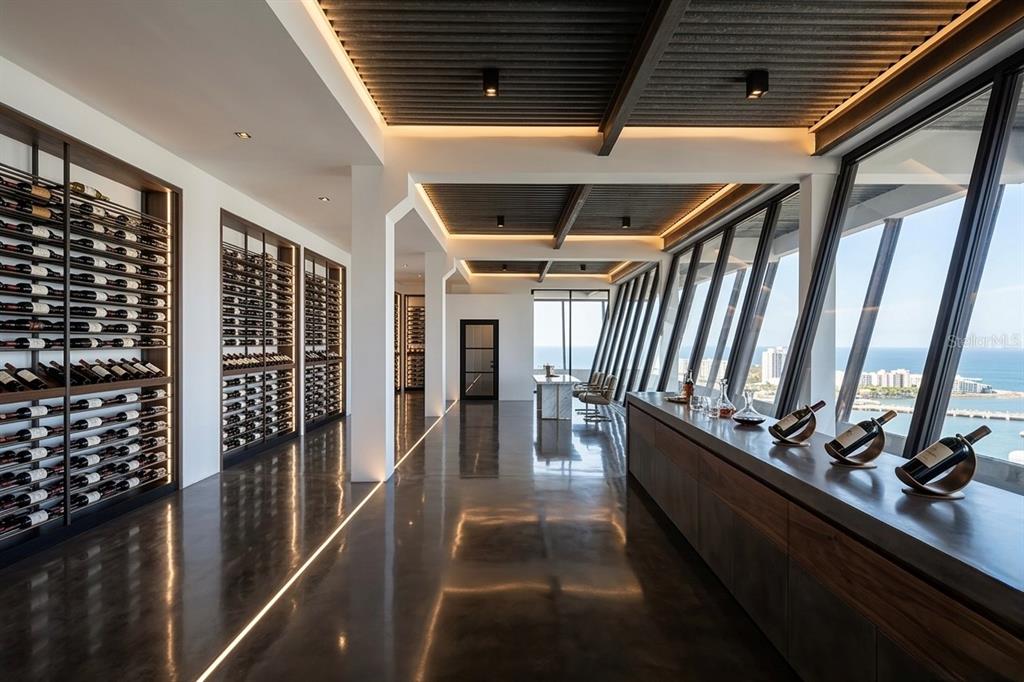 A modern wine room features floor-to-ceiling racks, polished concrete floors, and expansive ocean views — 602 MANUEL FERNÁNDEZ JUNCOS AVENUE UNIT 27, SAN JUAN, PR