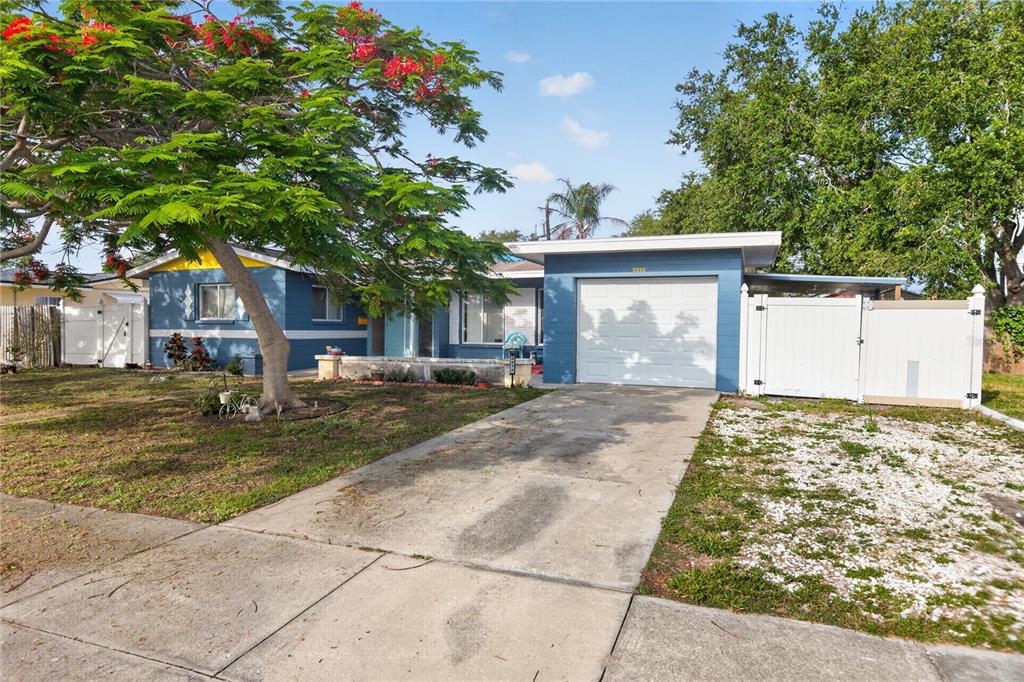 A blue single-story house with a white garage door, concrete driveway, and a large tree — 3232 59TH WAY N, ST PETERSBURG, FL