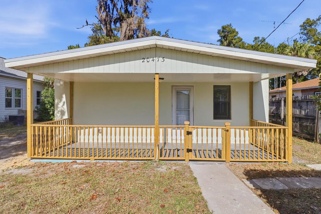 A single-story house features a covered front porch with a wooden railing and gate — 20473 W MCKINNEY AVENUE, DUNNELLON, FL