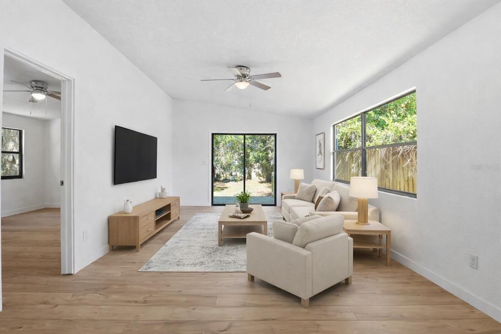 A living room features light wood flooring, a white sofa, a television, and sliding doors — 20473 W MCKINNEY AVENUE, DUNNELLON, FL