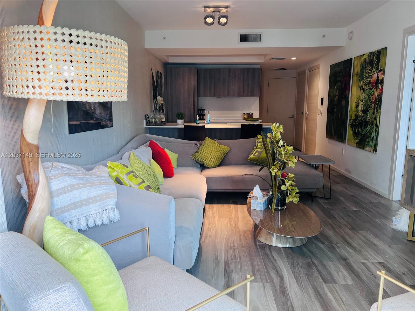 A living room with a gray sectional sofa, a woven floor lamp, and an open kitchen — 801 S Miami Ave # 3608, Miami FL 33130, MIAMI, FL