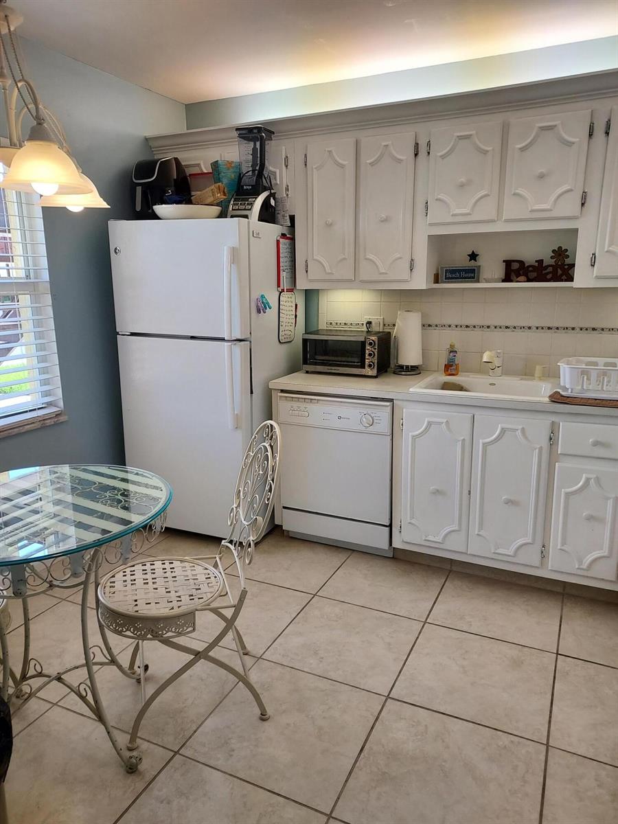 A kitchen features white cabinets, a white refrigerator, a dishwasher, and a small dining table — 717 S Us Highway 1 # 206, Jupiter FL 33477, JUPITER, FL