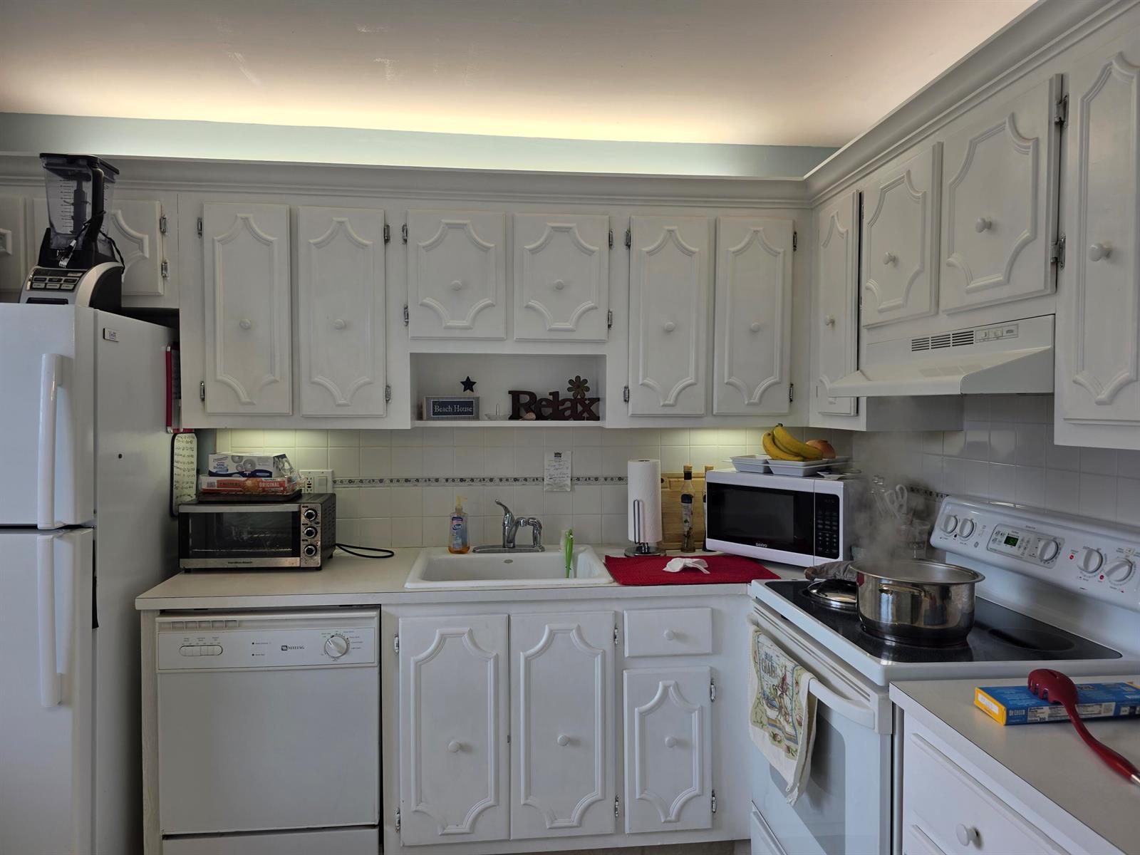 A kitchen featuring white cabinets, white appliances, a tiled backsplash, and a stainless steel sink — 717 S Us Highway 1 # 206, Jupiter FL 33477, JUPITER, FL