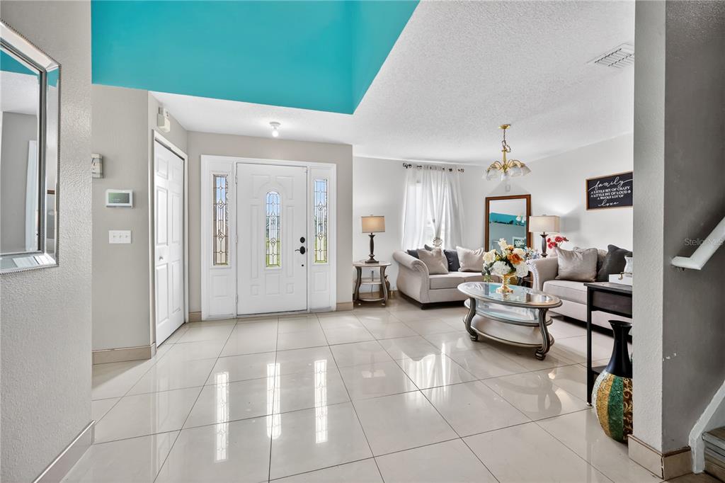 A bright entryway with light tile flooring leads into a living room with neutral furniture — 1945 MYAKKA COURT, KISSIMMEE, FL