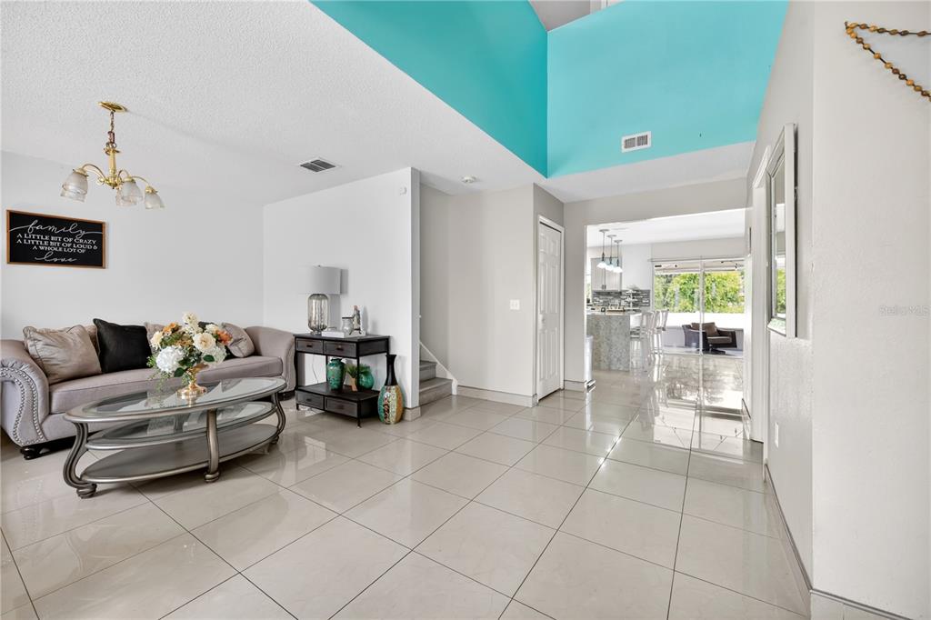 A living room with light tile flooring, a grey sofa, and a high teal-accented ceiling — 1945 MYAKKA COURT, KISSIMMEE, FL