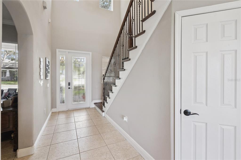A bright entryway features tiled floors, a staircase with dark wood railings, and a front door — 1727 SOUTHERN OAK LOOP, MINNEOLA, FL