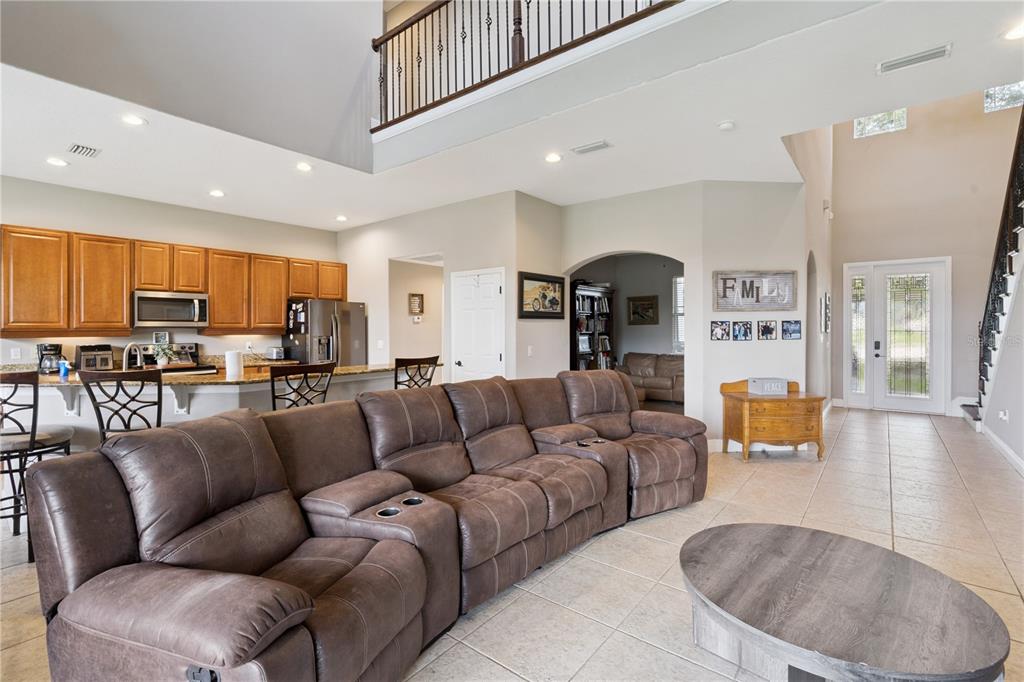 A spacious open-concept living room features a large brown sectional sofa, tile flooring, and a kitchen — 1727 SOUTHERN OAK LOOP, MINNEOLA, FL