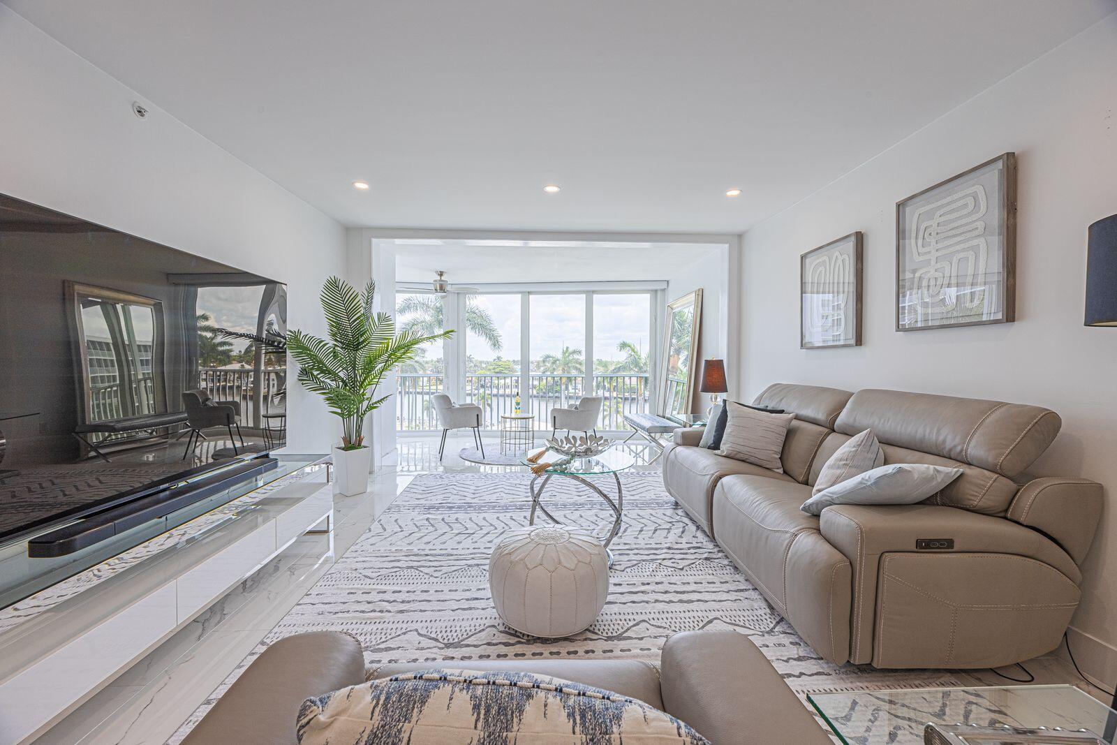 A modern living room features a large television, leather sofa, patterned rug, and balcony view — 3224 S Ocean Boulevard # 612b, Highland Beach FL 33487, HIGHLAND BEACH, FL