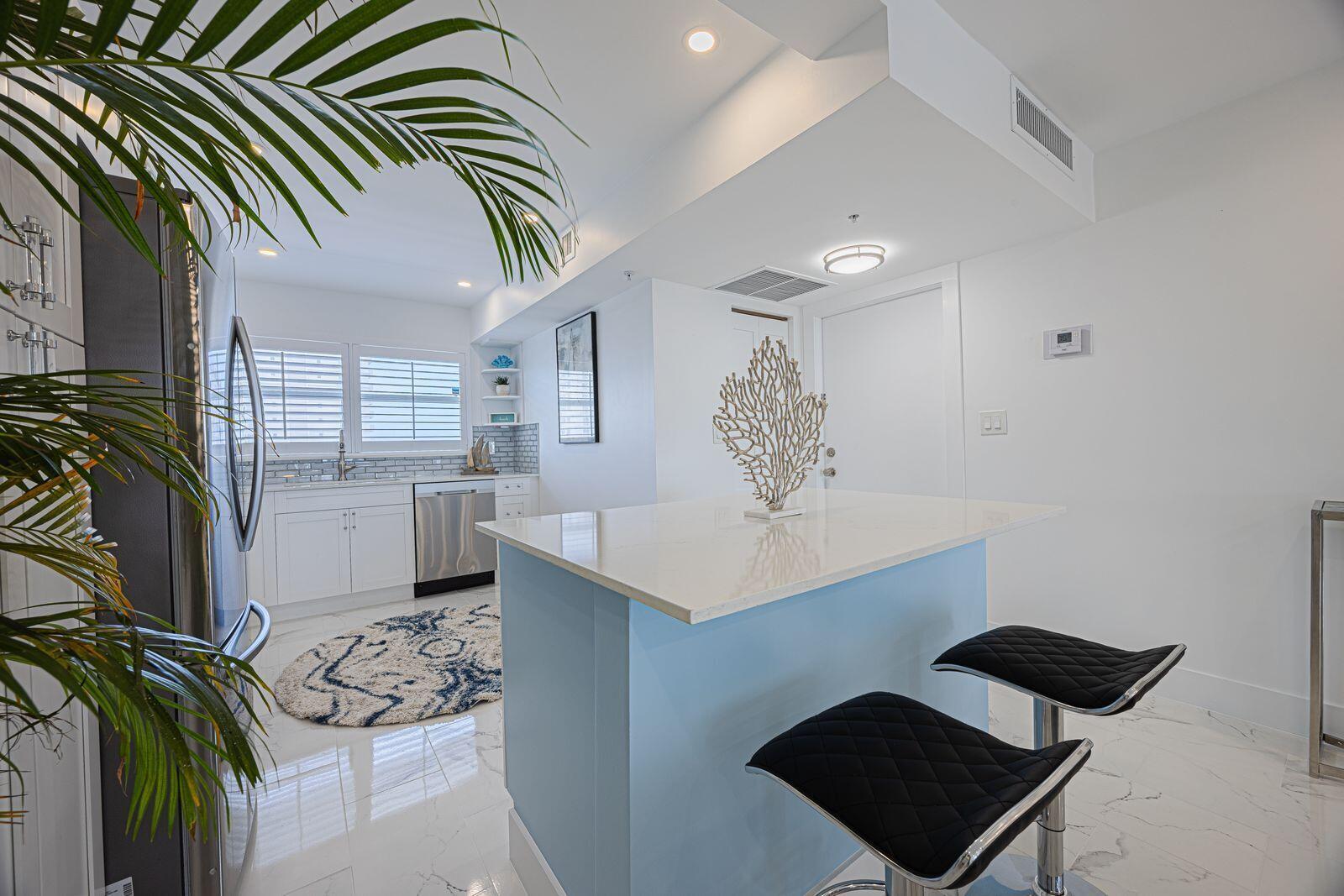 A kitchen features white cabinets, a light blue island with bar stools, and marble flooring — 3224 S Ocean Boulevard # 612b, Highland Beach FL 33487, HIGHLAND BEACH, FL