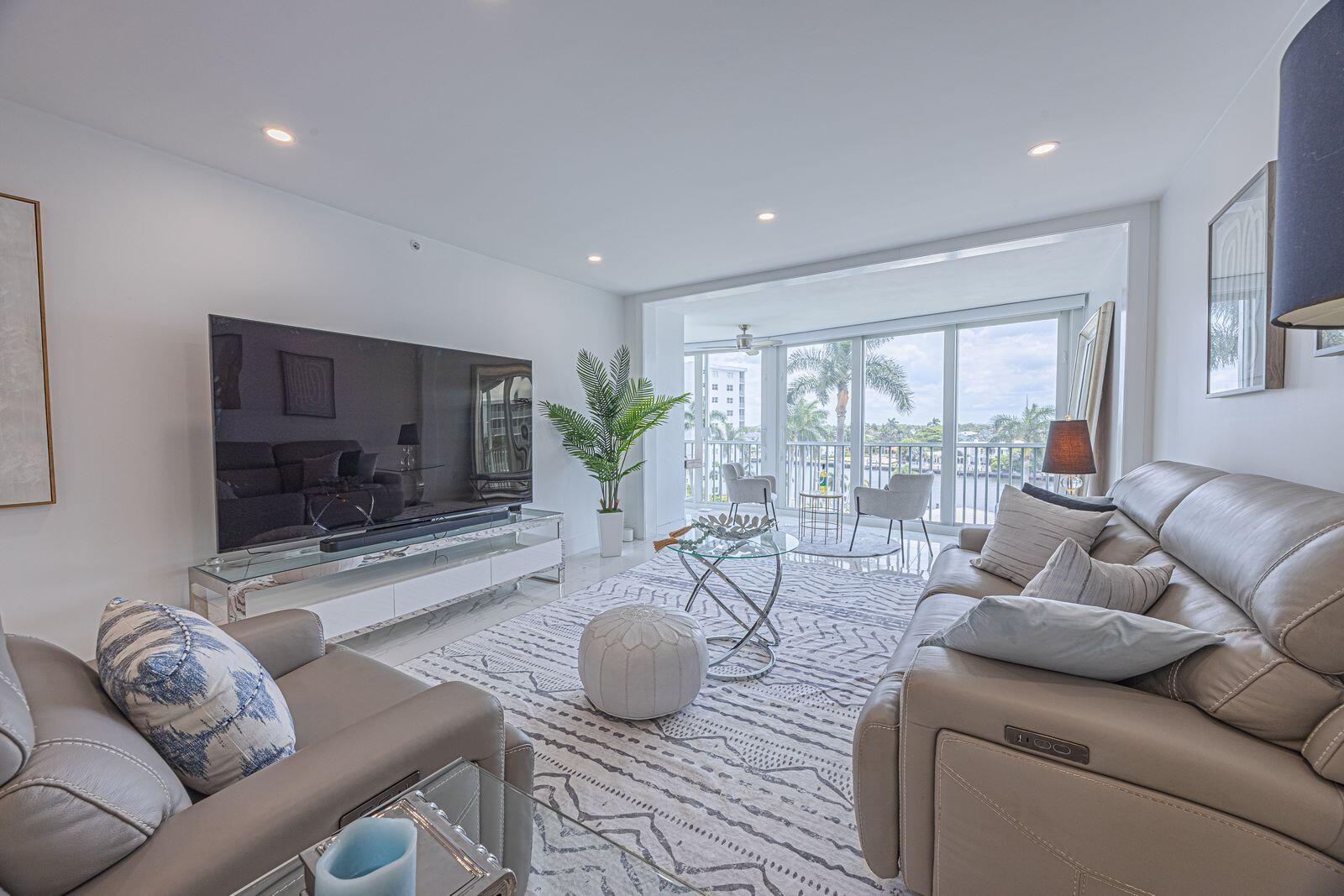 A modern living room features a large television, leather sofas, and a balcony with water views — 3224 S Ocean Boulevard # 612b, Highland Beach FL 33487, HIGHLAND BEACH, FL