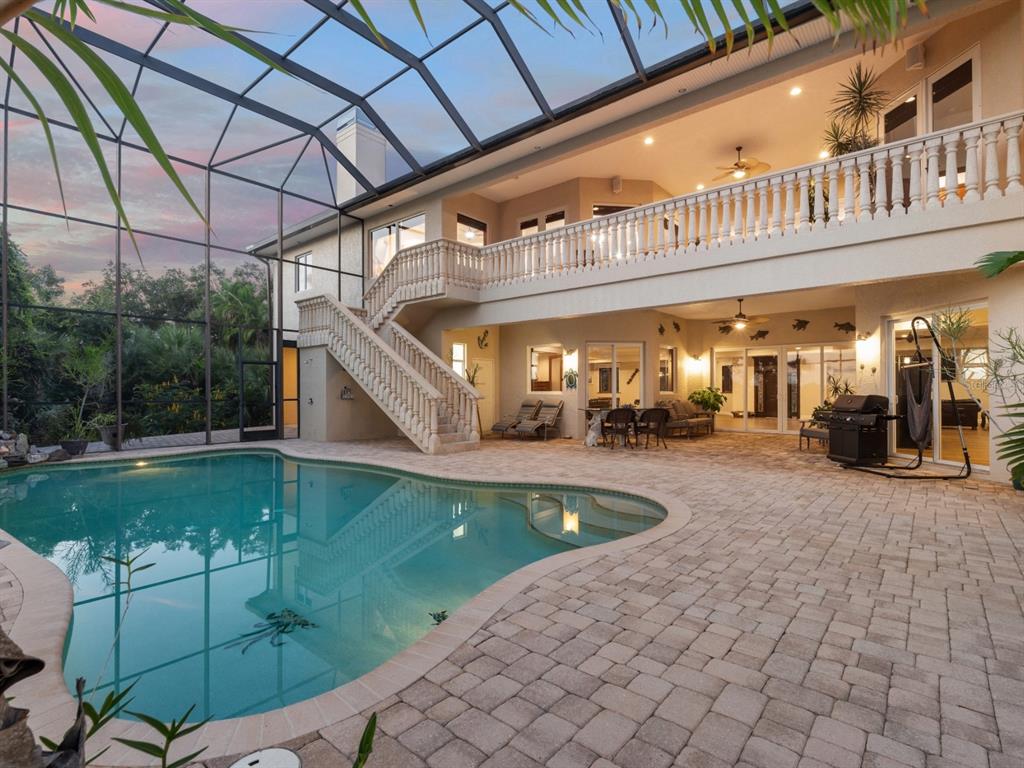 A two-story house exterior features a screened-in pool, stone patio, and an outdoor staircase — 1930 BAYSHORE DRIVE, ENGLEWOOD, FL
