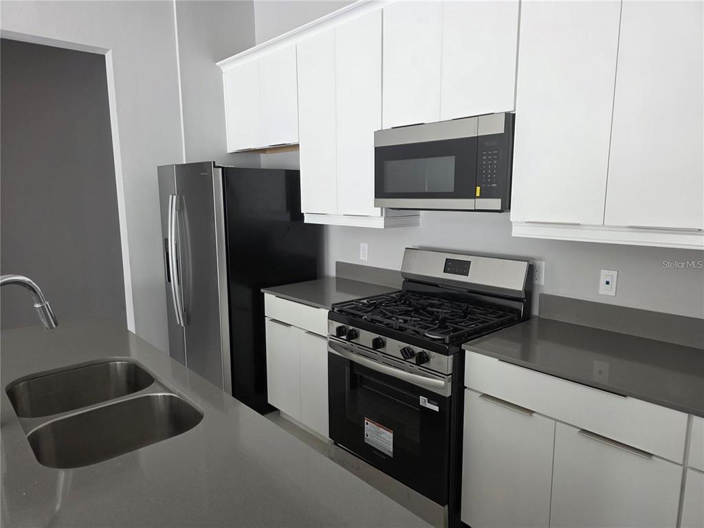 A modern kitchen features white cabinets, stainless steel appliances, and gray quartz countertops — 7760 SANDY RIDGE DRIVE UNIT 112, REUNION, FL