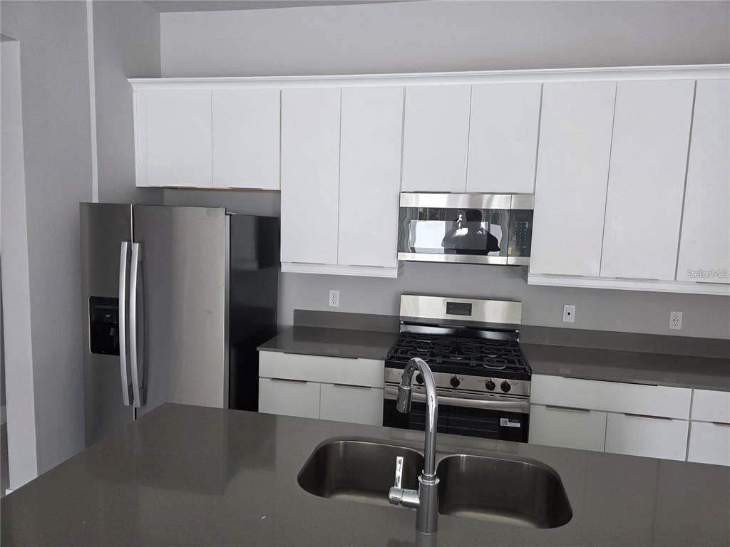 A kitchen features white cabinets, stainless steel appliances, and a gray island with a sink — 7760 SANDY RIDGE DRIVE UNIT 112, REUNION, FL