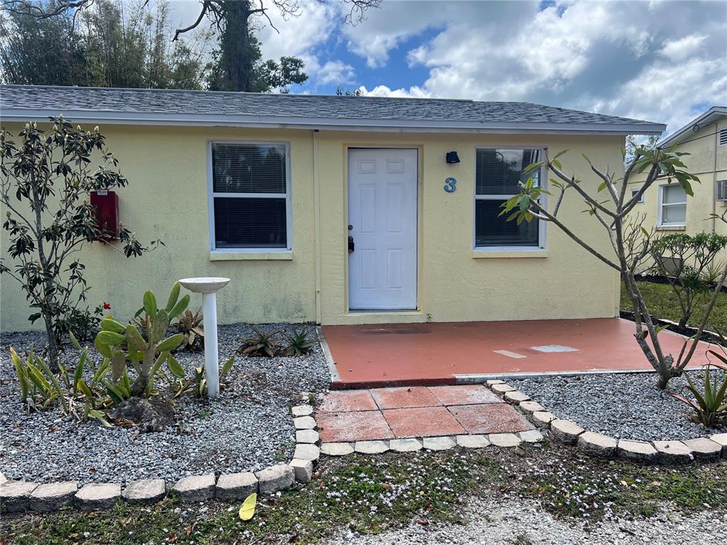 A yellow single-story building features a white front door, two windows, and a small patio — 255 PINEAPPLE STREET UNIT 3, ENGLEWOOD, FL