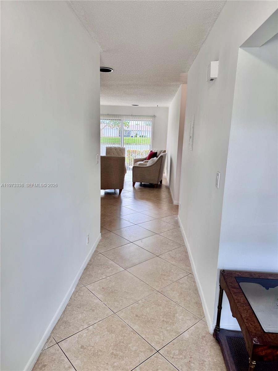 A tiled hallway leads to a living area with armchairs and a sliding glass door — 8838 Bella Vista Dr, Boca Raton FL 33433, BOCA RATON, FL