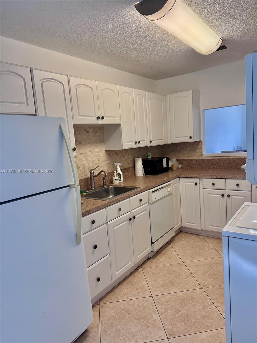 This kitchen features white cabinets, a speckled countertop, a stainless steel sink, and tile flooring — 8838 Bella Vista Dr, Boca Raton FL 33433, BOCA RATON, FL