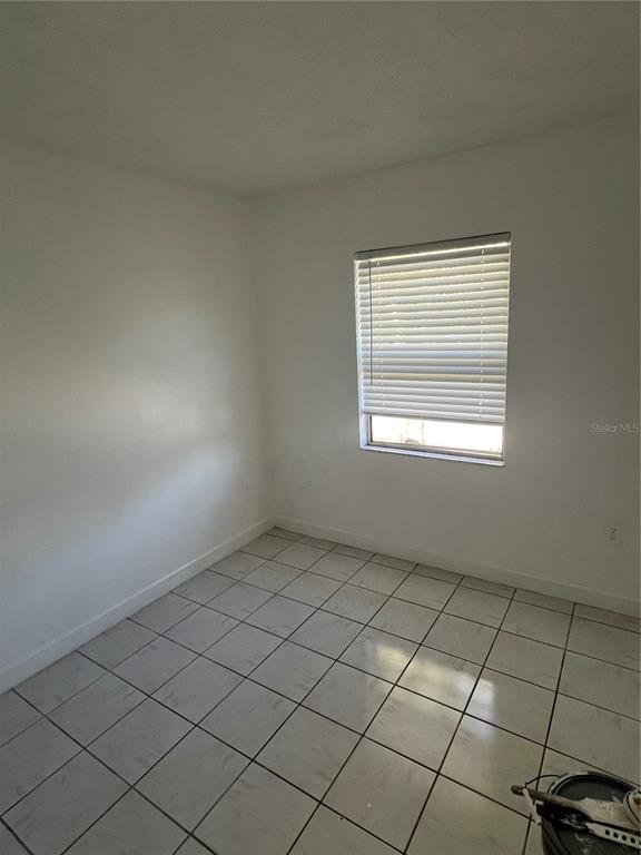 A small, empty room features white walls, a window with blinds, and light-colored tiled flooring — 1908 HONOUR RD UNIT 3, ORLANDO, FL