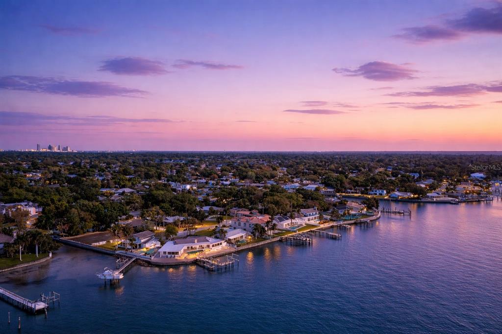 An aerial view of a waterfront residential neighborhood at sunset with a distant city skyline — 2970 68TH AVENUE S, ST PETERSBURG, FL