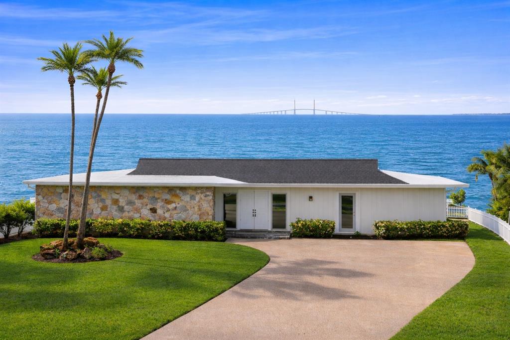 A single-story house with a stone facade and white siding sits on a grassy waterfront lot — 2970 68TH AVENUE S, ST PETERSBURG, FL